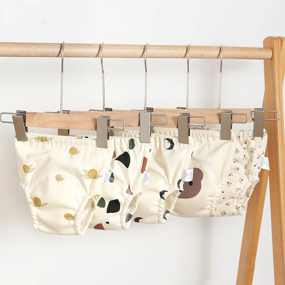 Two baby diapers with cartoon designs hanging on a wooden rack against a white background.