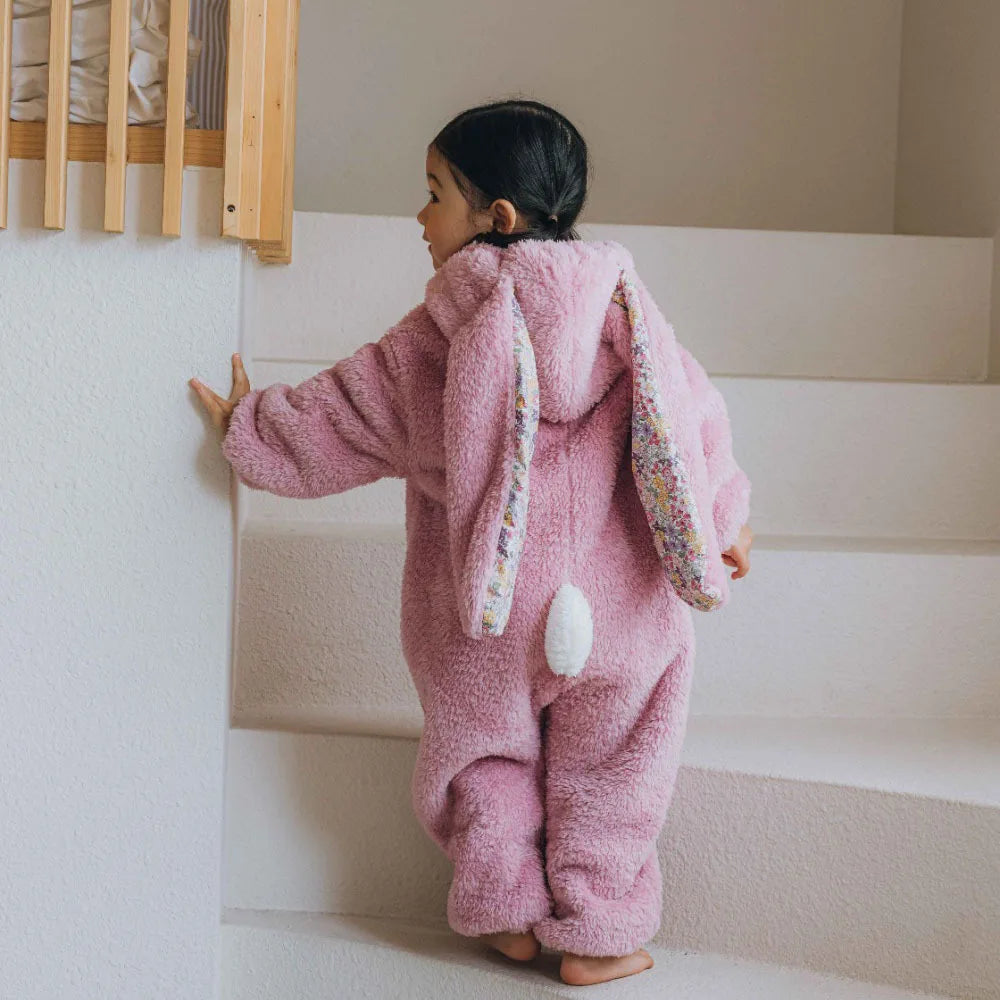 Child in a pink bunny onesie standing on a staircase.