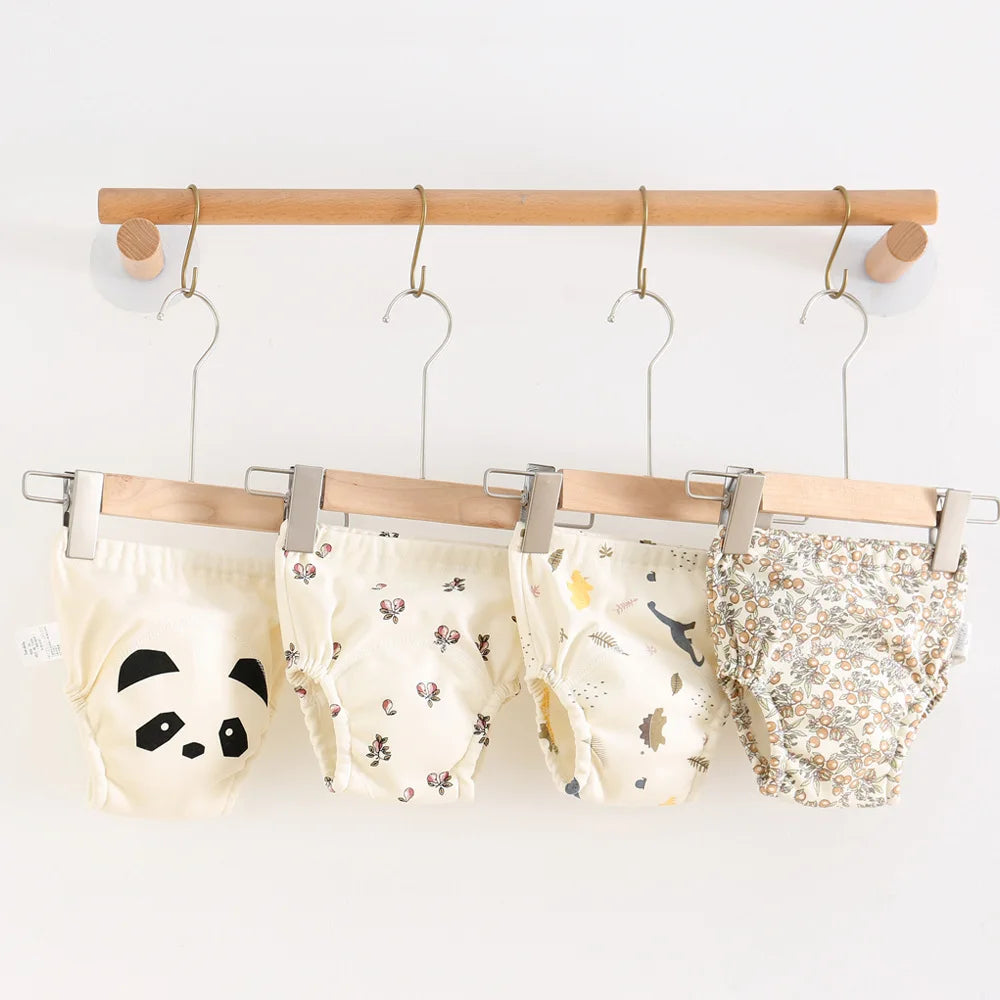 Four baby bloomers with different patterns hanging on a rack against a white background