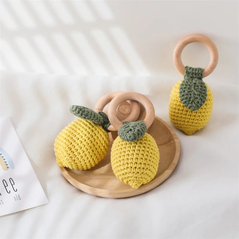 Two crochet lemon toys with wooden rings on a white surface.
